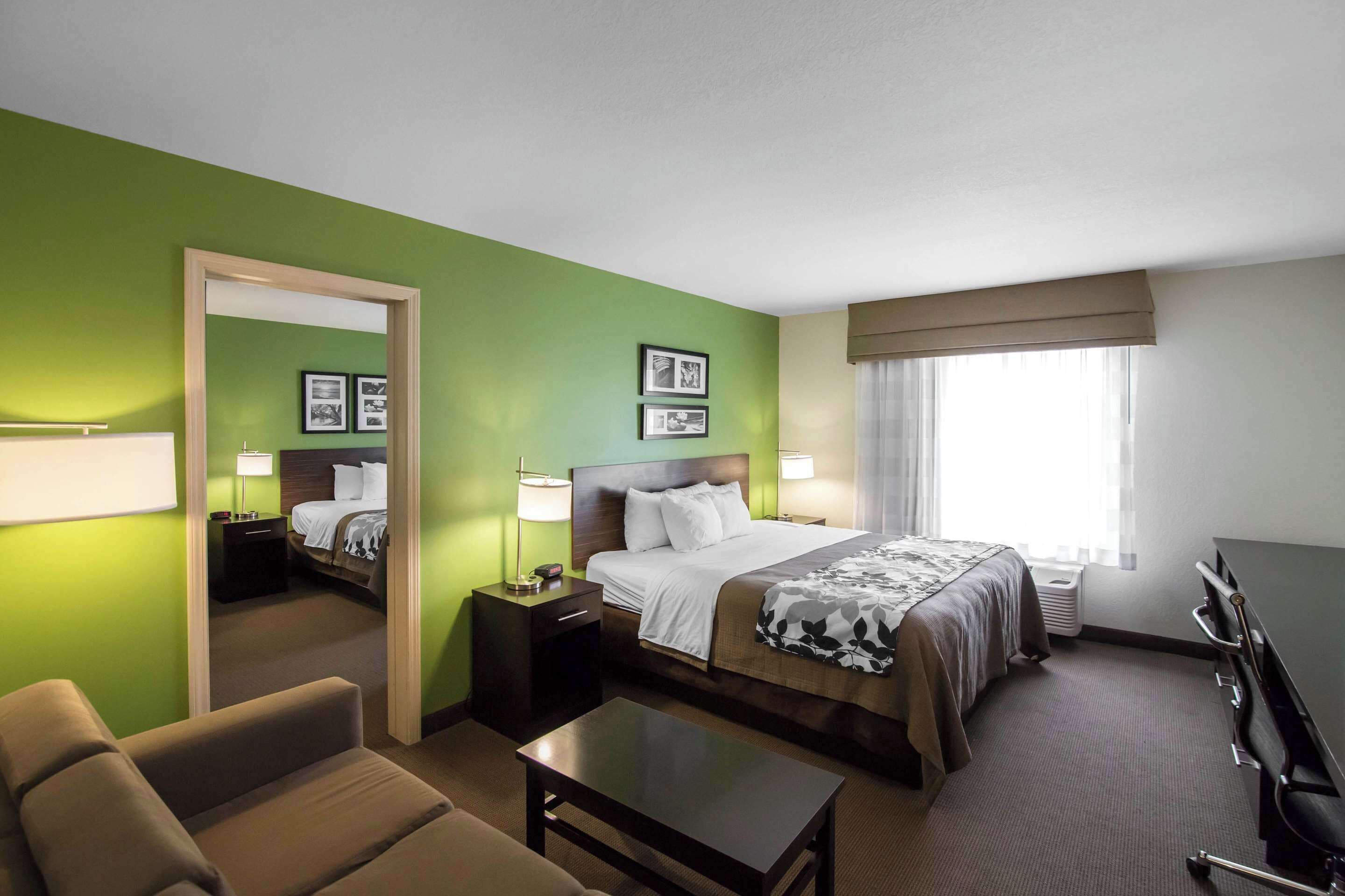 Una habitación de hotel con cama, mesitas de noche, escritorio, silla y un espejo grande.