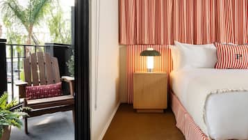 Una habitación de hotel con cama, mesita de noche con lámpara, una silla y vistas al exterior.