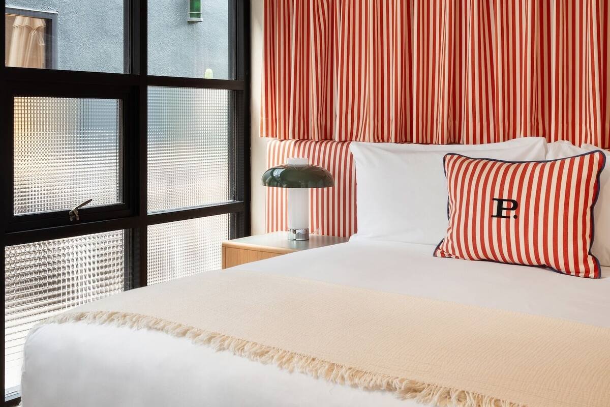 A hotel room with a large bed, striped curtains, and a view through a window with a metal grill.