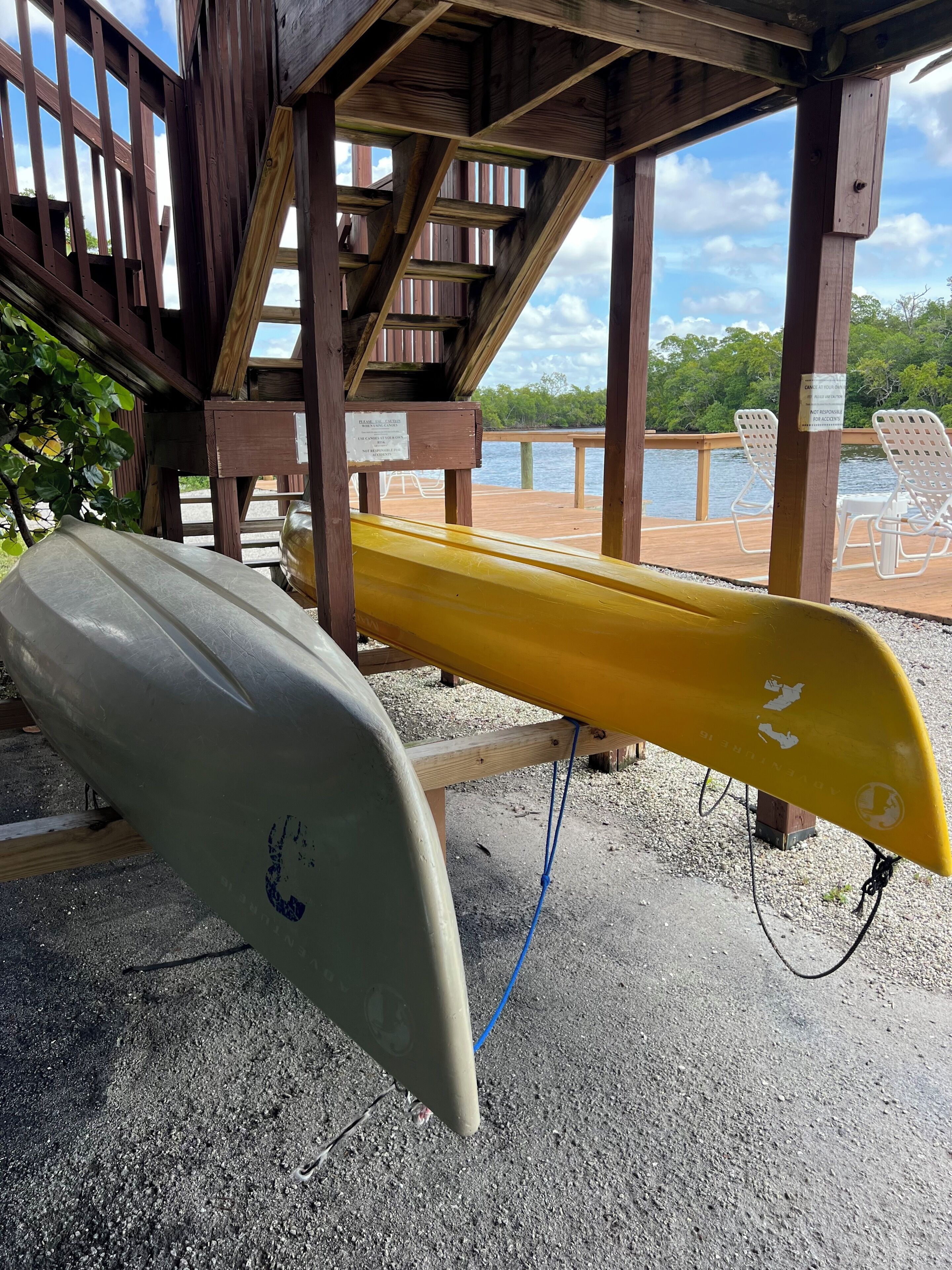 Una terraza de madera con dos tablas de surf, una blanca y otra amarilla, y un cartel que advierte sobre un suelo resbaladizo.