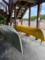 Una terraza de madera con dos tablas de surf, una blanca y otra amarilla, y un cartel que advierte sobre un suelo resbaladizo.