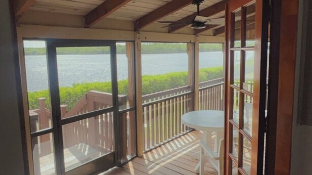 Een houten terras met een glazen deur die leidt naar een balkon met uitzicht op een wateroppervlak.