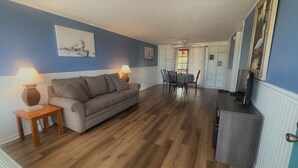 Een woonkamer met een bank, twee lampen, een eettafel met stoelen en een tv-meubel.