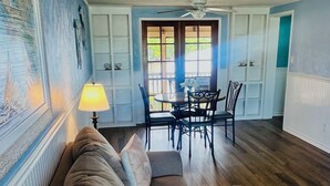 Een woonkamer met een bank, een eettafel met stoelen, een plafondventilator en een raam met uitzicht op groen.