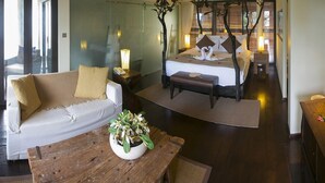 A modern hotel room with a bed, a sofa, a wooden table, and a decorative plant. - Dhevatara Beach Hotel & Spa (Praslin Island)