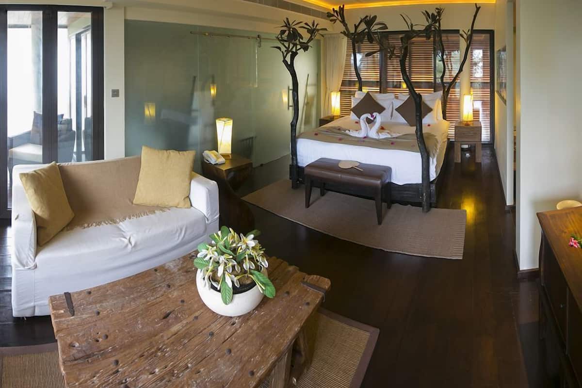 Une chambre d’hôtel moderne avec un lit, un canapé, une table en bois et une plante décorative.