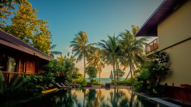 A pool area with lounge chairs, palm trees, and a view of the sea. - Dhevatara Beach Hotel & Spa (Praslin Island)