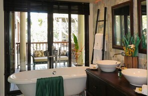 A bathroom with a freestanding bathtub, two sinks, a large mirror, and a view of a balcony with outdoor furniture.