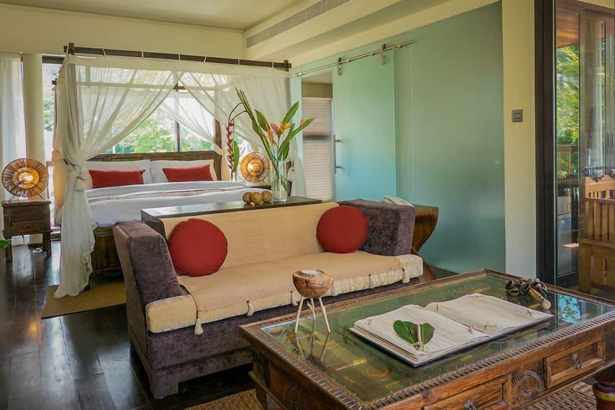 Une chambre à coucher comprenant un lit, un canapé, une table basse en verre et une table de chevet avec une lampe.