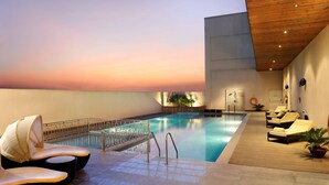 A rooftop pool area with lounge chairs and a view of the sunset.