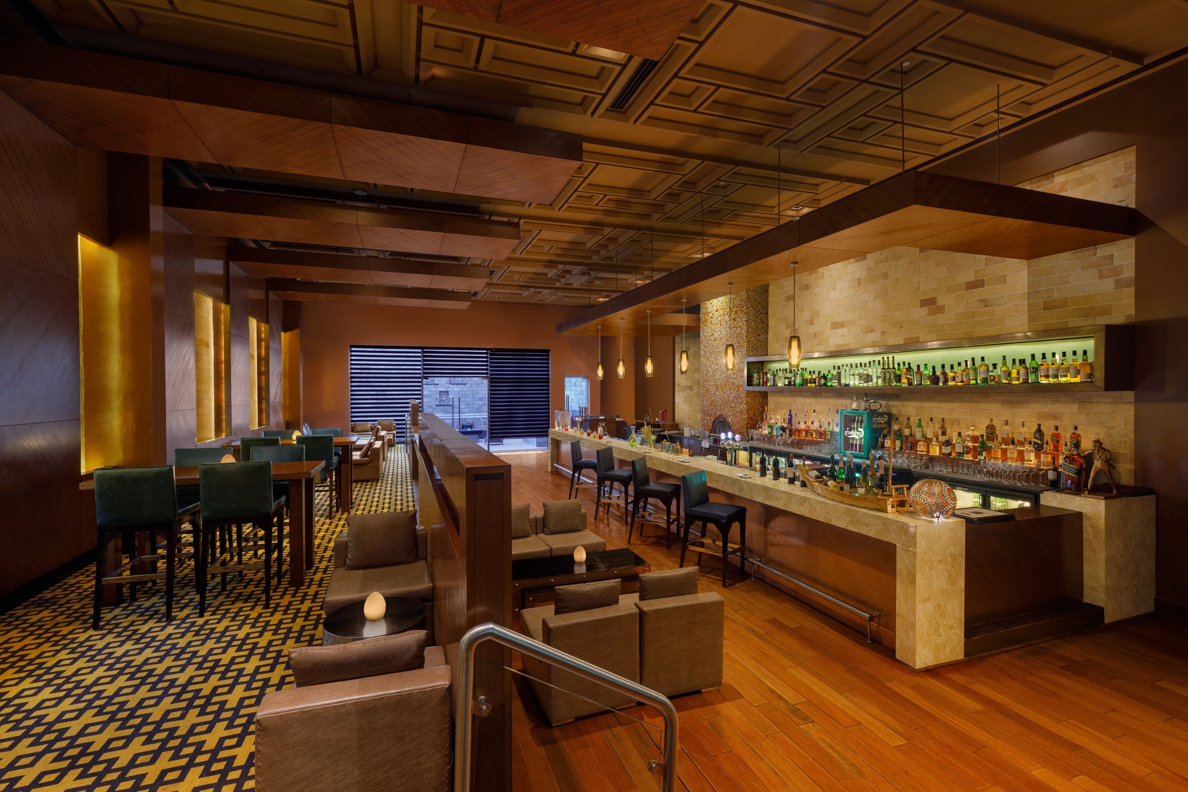 A bar area with a long counter, multiple seating options, and a variety of bottles on shelves.