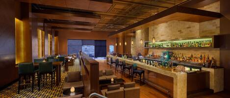 Uma área de bar com balcão extenso, diversas opções de assento e variedade de garrafas nas prateleiras.