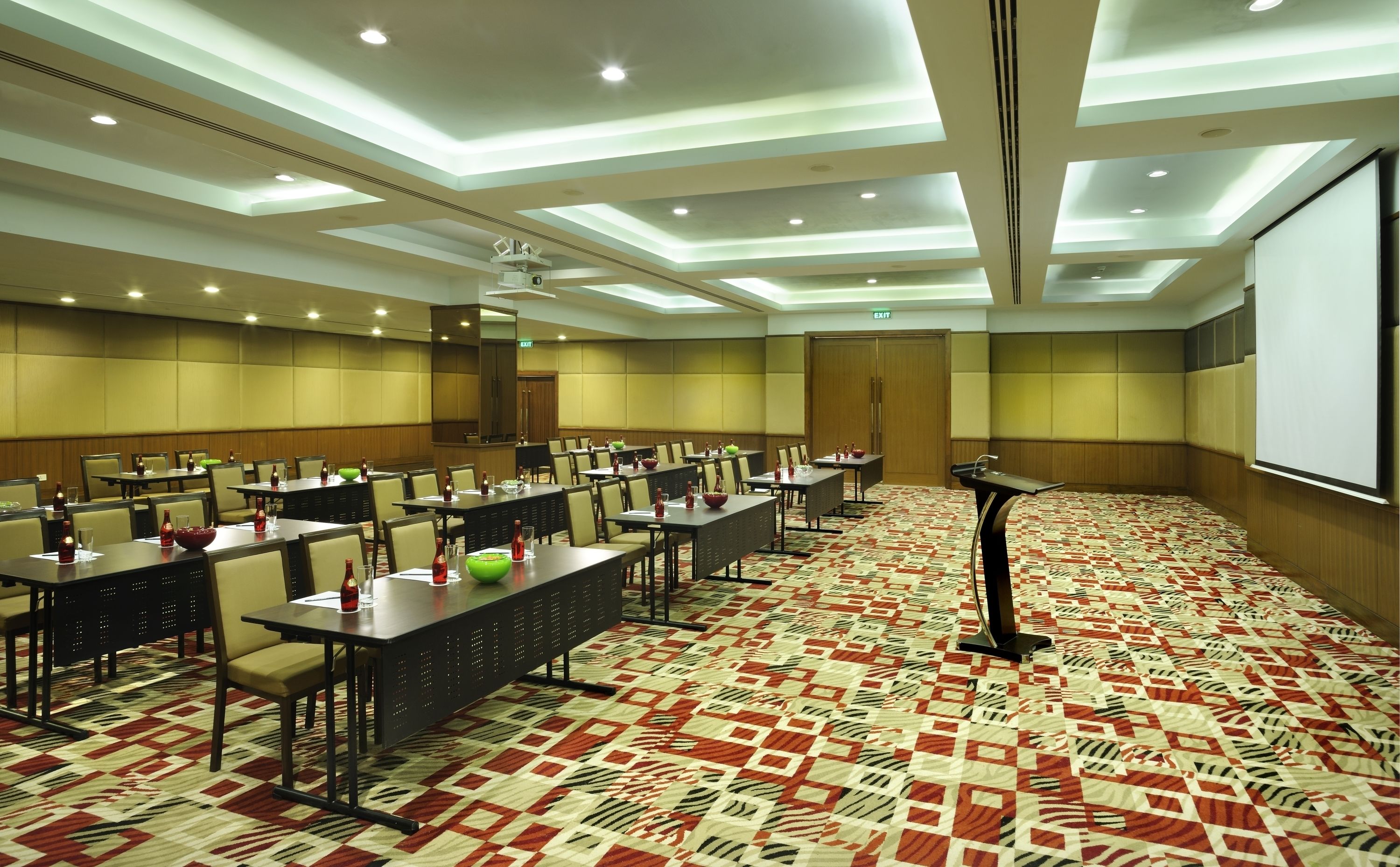 A conference room with tables, chairs, a podium, and a projector screen.