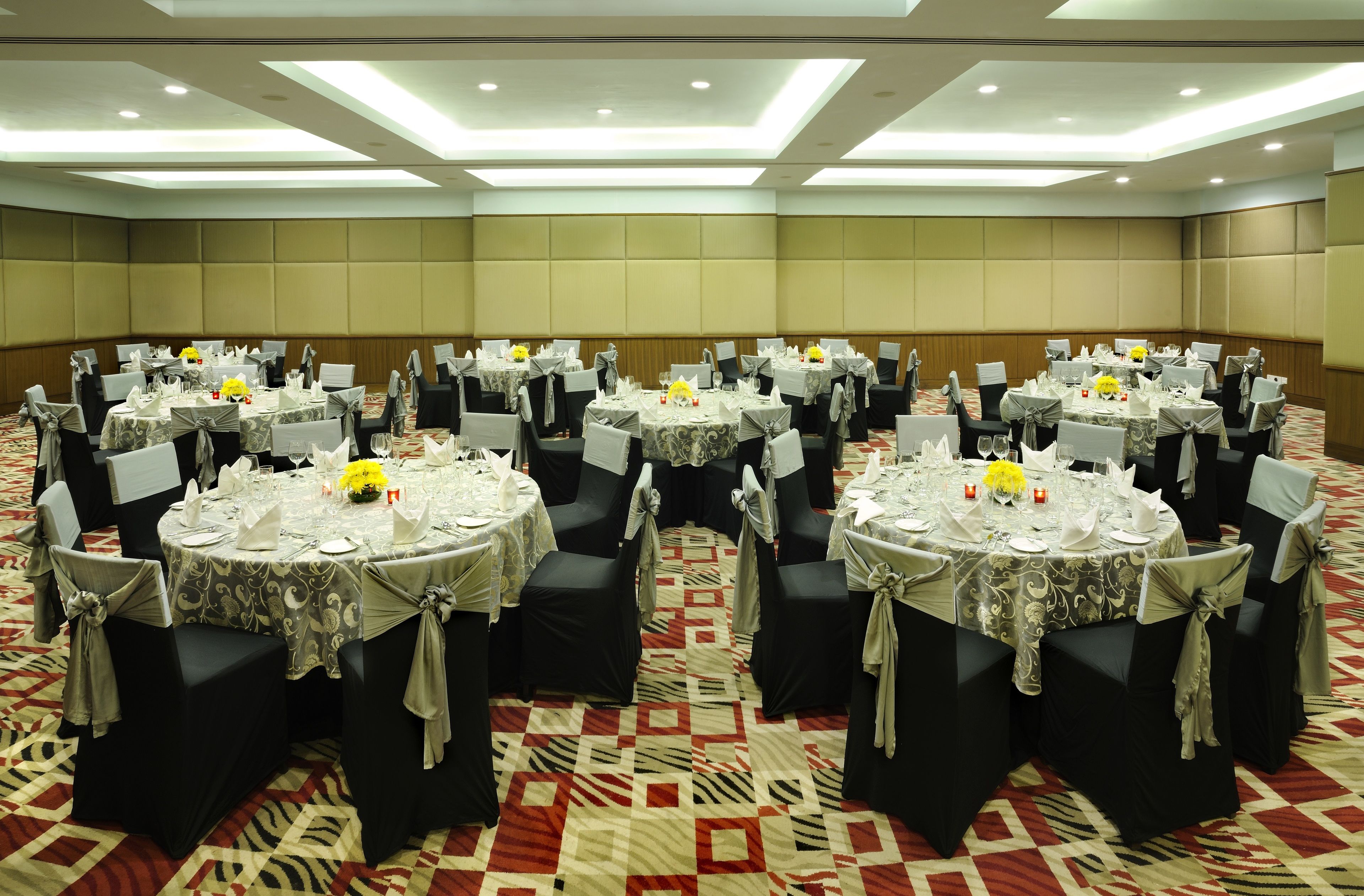 A banquet hall with multiple round tables, each set with white tablecloths, black chairs, and yellow centerpieces.