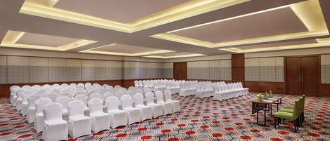 Un salón de conferencias con filas de sillas blancas, una alfombra estampada e iluminación empotrada en el techo.