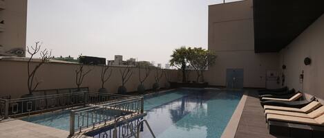 A rooftop pool with lounge chairs, a diving board, and a clear view of the city skyline.