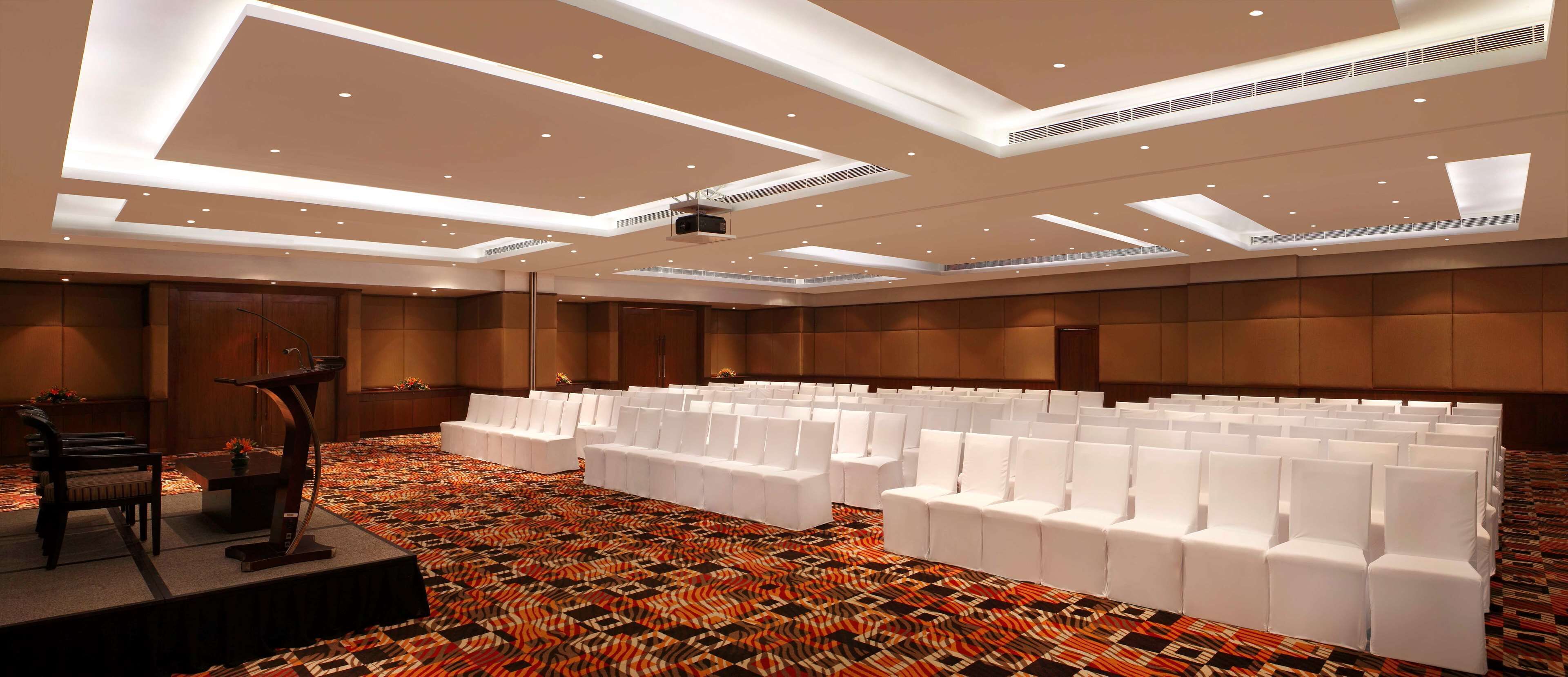 A conference room with rows of white chairs, a podium, and a carpeted floor.