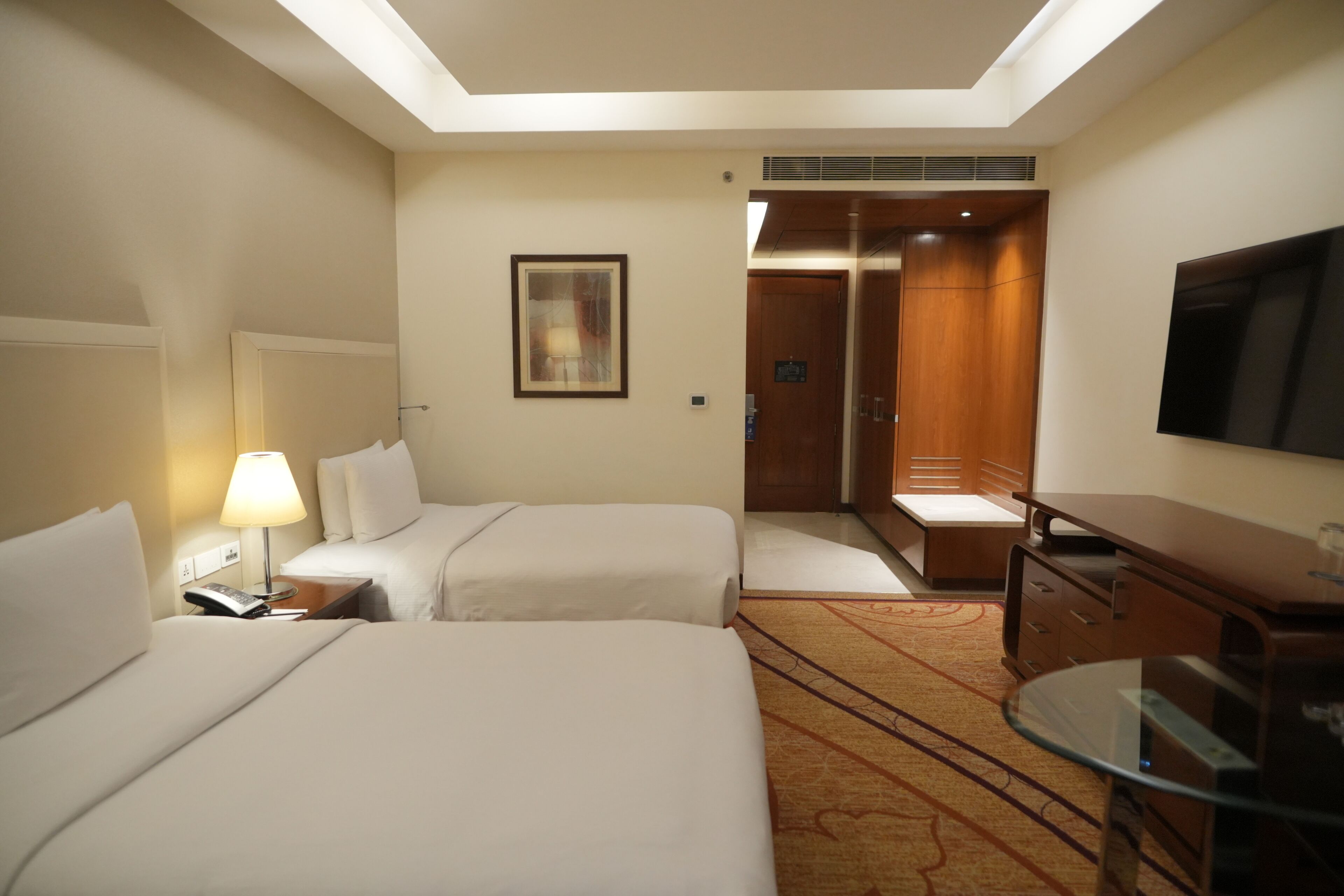 A hotel room with two beds, a desk, a television, and a door leading to a bathroom.