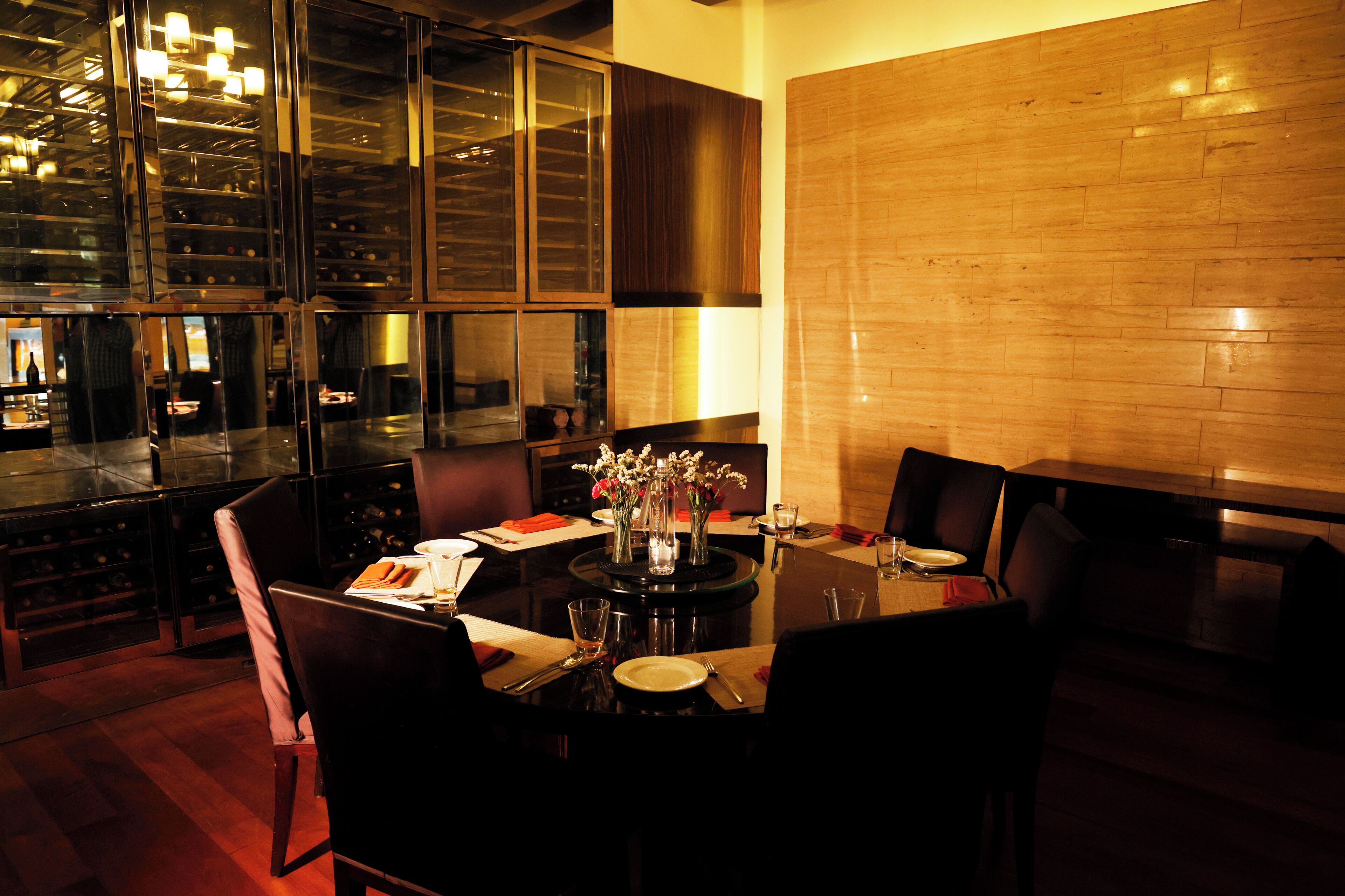 A restaurant with a dark wood table set for two, a vase with flowers, and a brick wall.