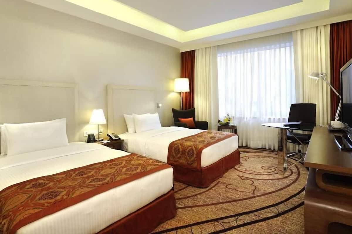 A hotel room with two beds, a desk, a chair, a TV, and a window with curtains.