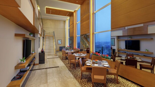 A modern hotel lobby with a staircase, dining area, and large windows.