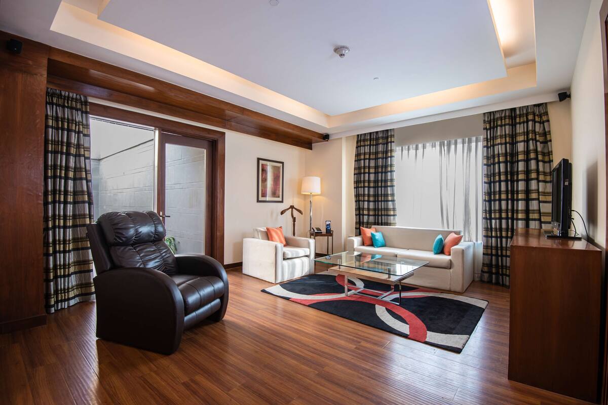 A modern living room with a leather chair, white sofas, a glass coffee table, and a wooden floor.
