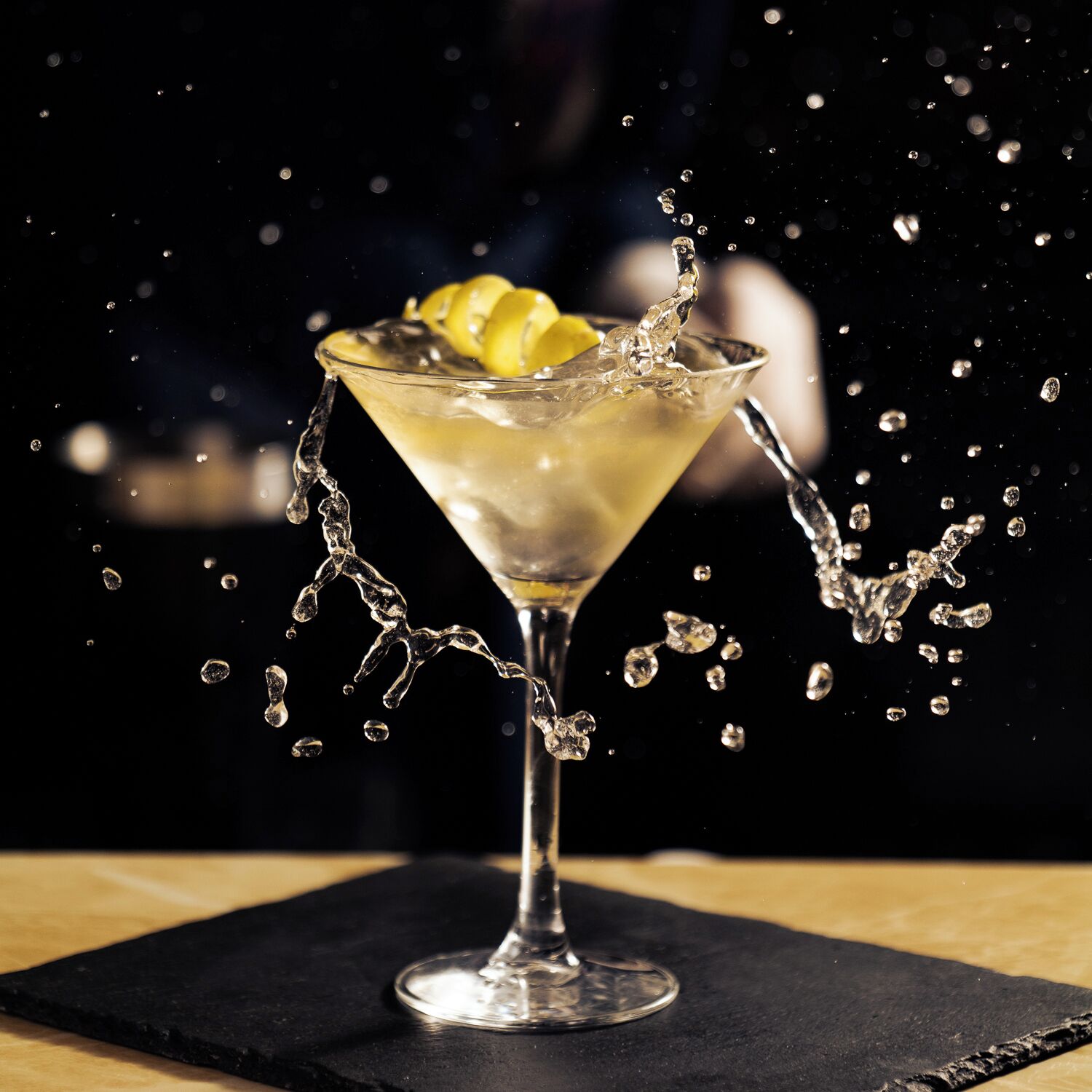 Una copa de martini con una rodaja de limón sobre un posavasos negro.