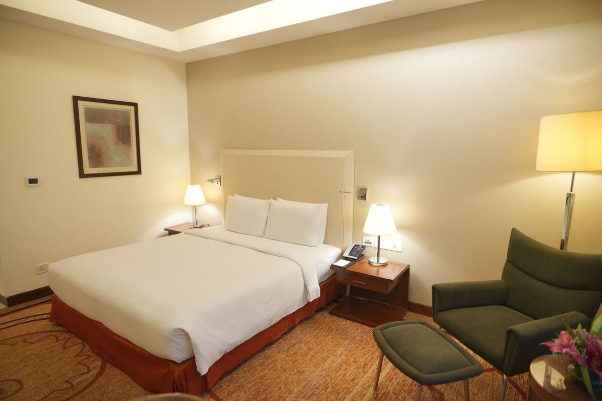 A hotel room with a large bed, two bedside tables with lamps, a chair, and a small table with a vase.