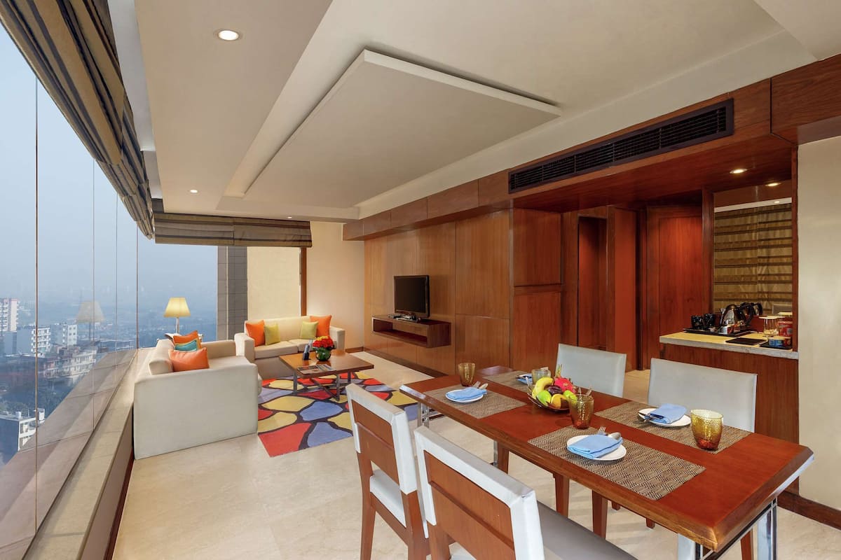 A modern living area with a dining table set for four, a sofa, a TV, and a city view.