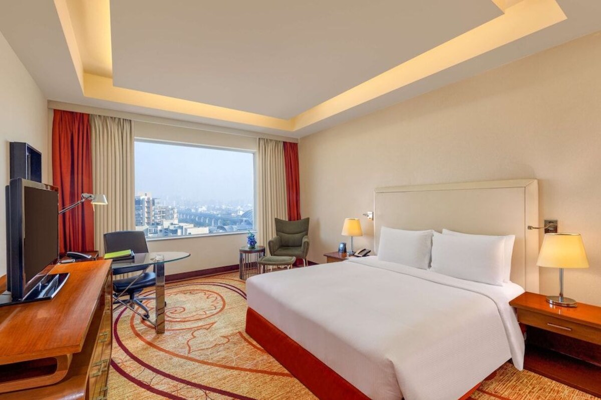 A hotel room with a large bed, a desk with a computer, a chair, a TV, and a view of the city.