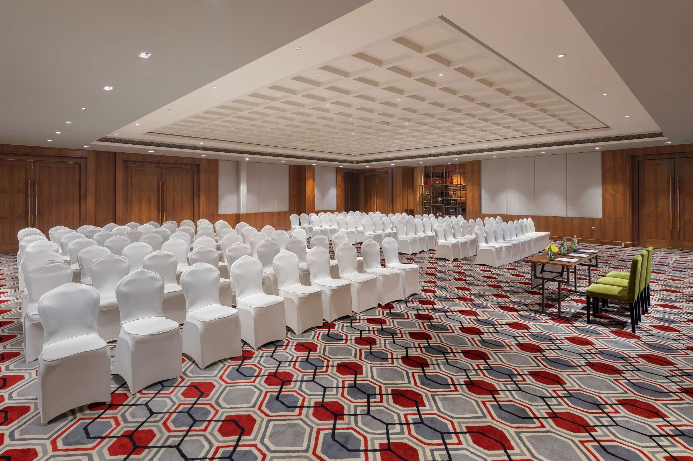 A large conference room with rows of white chairs, a patterned carpet, and wooden paneling on the walls.