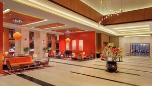 A spacious lobby with a red accent wall, a seating area with orange sofas, and a large vase of flowers.