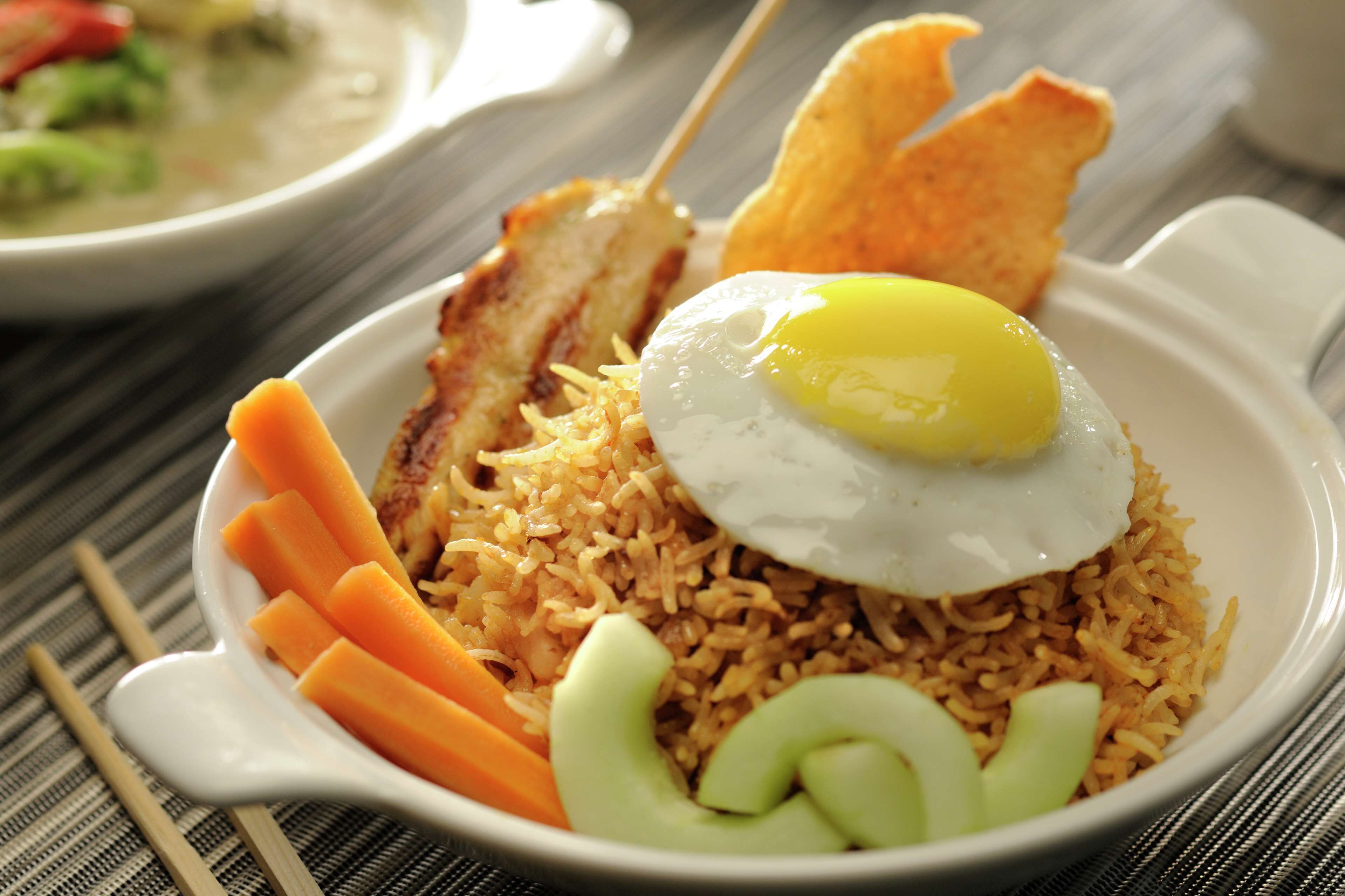 Un tazón de arroz frito con un huevo frito encima, acompañado de zanahorias y pepino en rodajas.