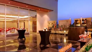 A hotel lobby with a checkered floor, a bar area with drinks, and a seating area with tables.