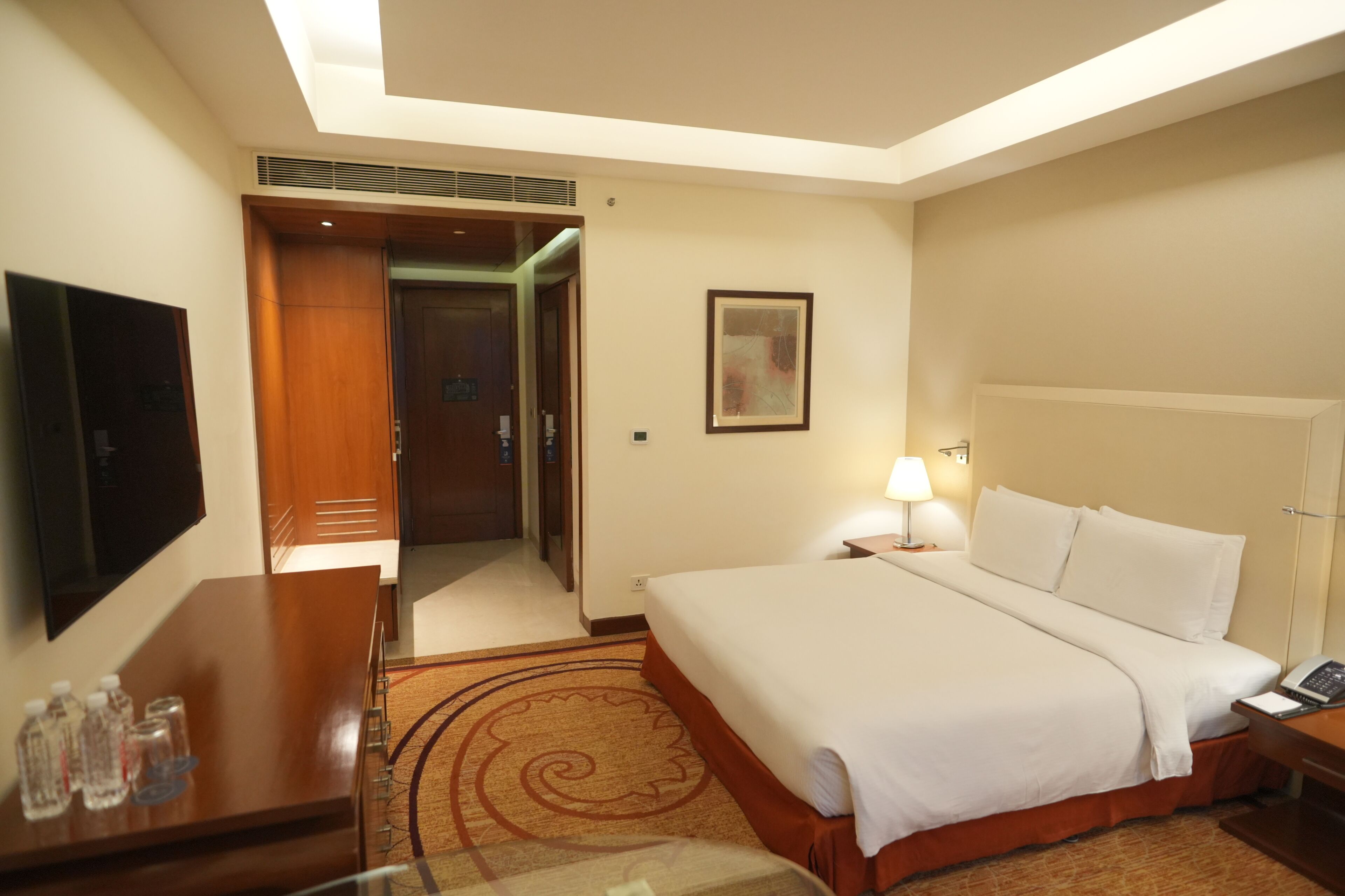 A hotel room with a bed, bedside table, lamp, and a television on a stand.