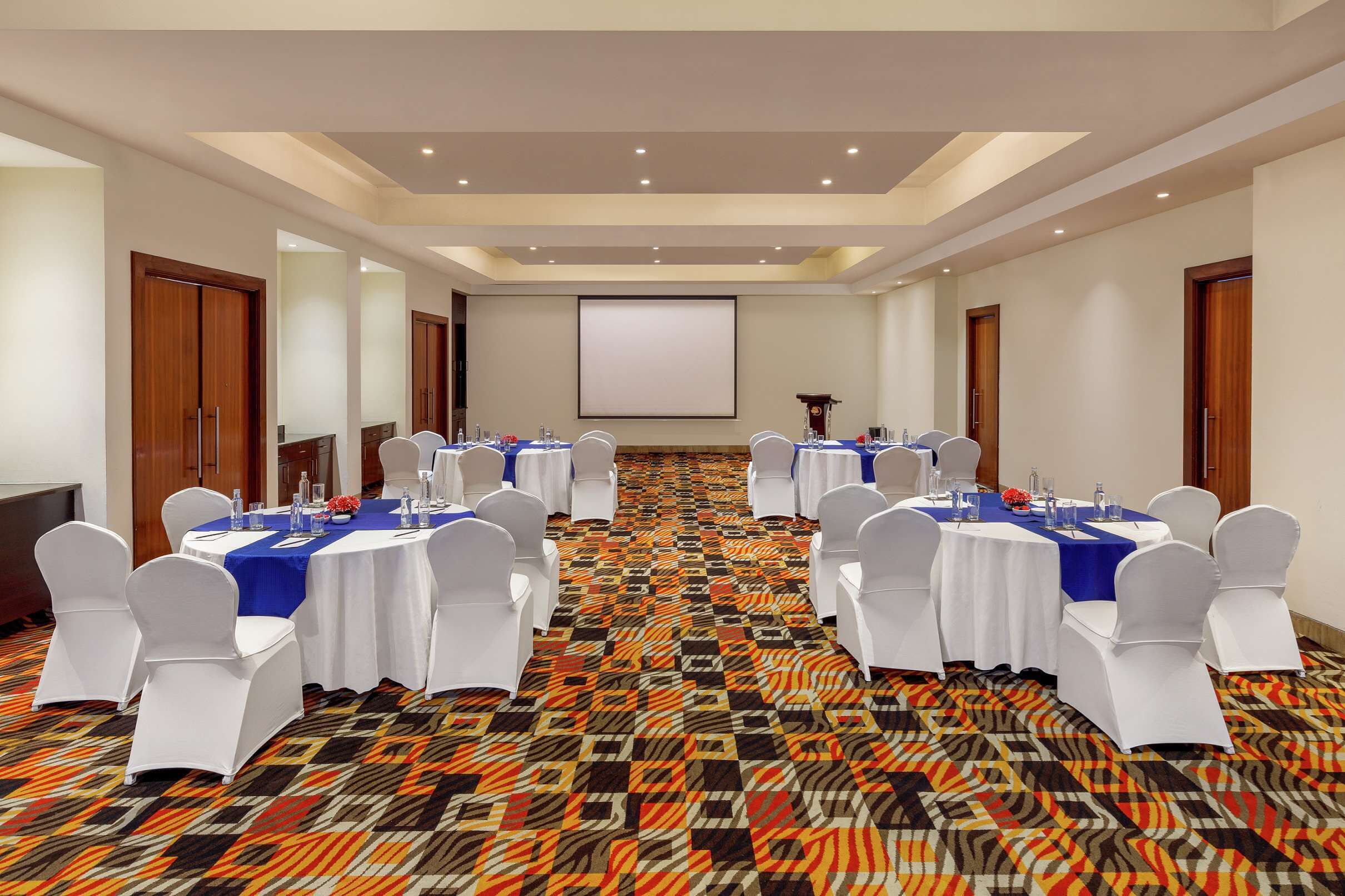 A conference room with tables set for a meeting, white chairs, and a projector screen.