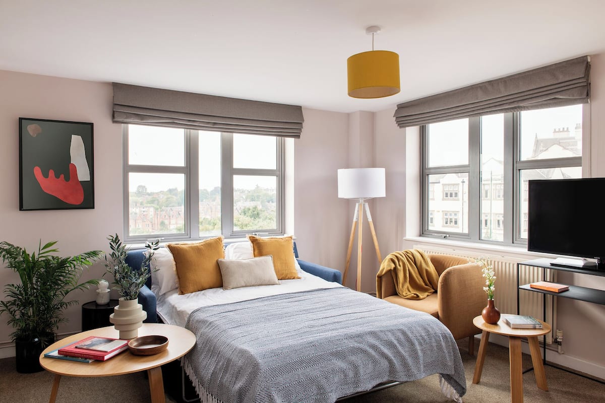 A modern hotel room with a bed, a desk, a chair, a TV, and large windows.