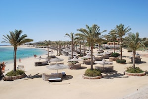 Un resort frente al mar con palmeras, sillas de playa y sombrillas.