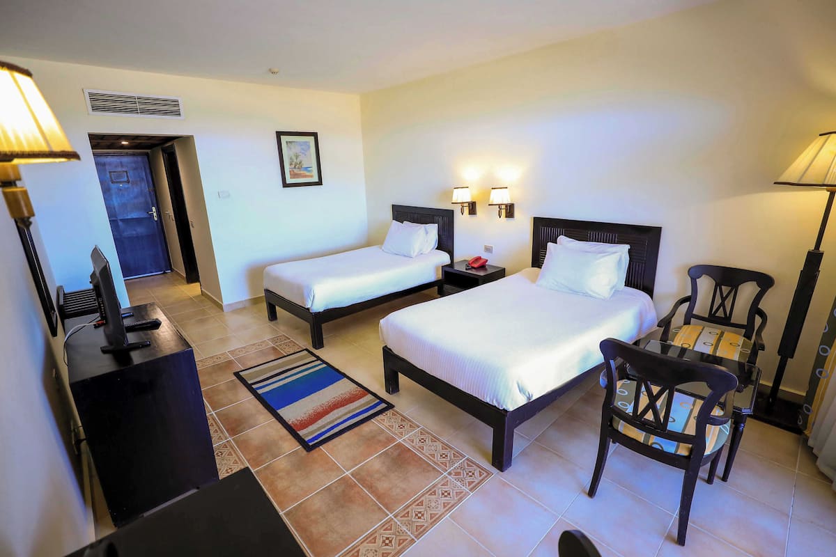 A hotel room with two beds, a desk, a chair, and a TV.