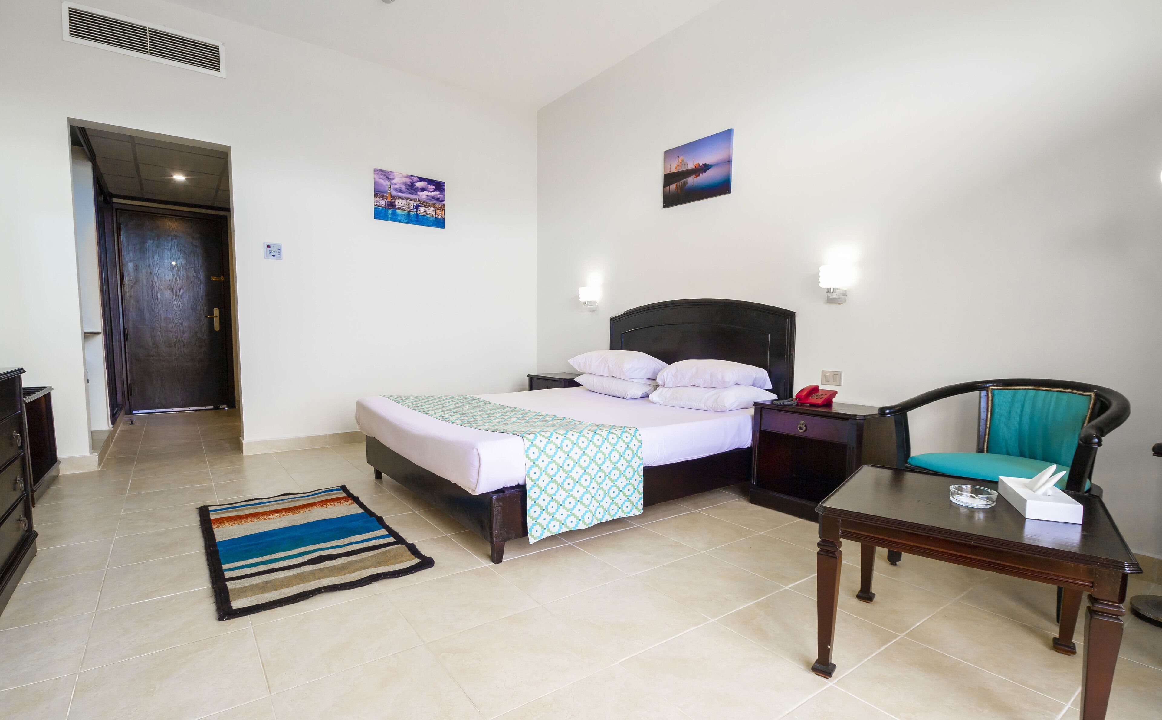 Habitación de hotel con cama, mesita de noche, silla y alfombra.