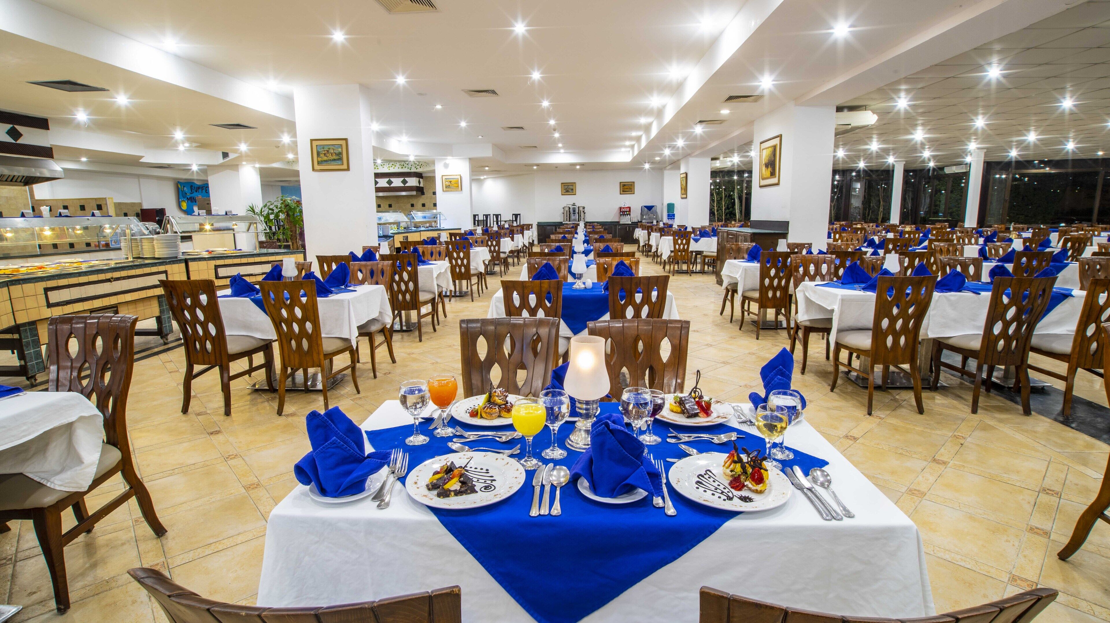 A large dining area with multiple tables and chairs, a buffet counter, and a kitchen in the background.