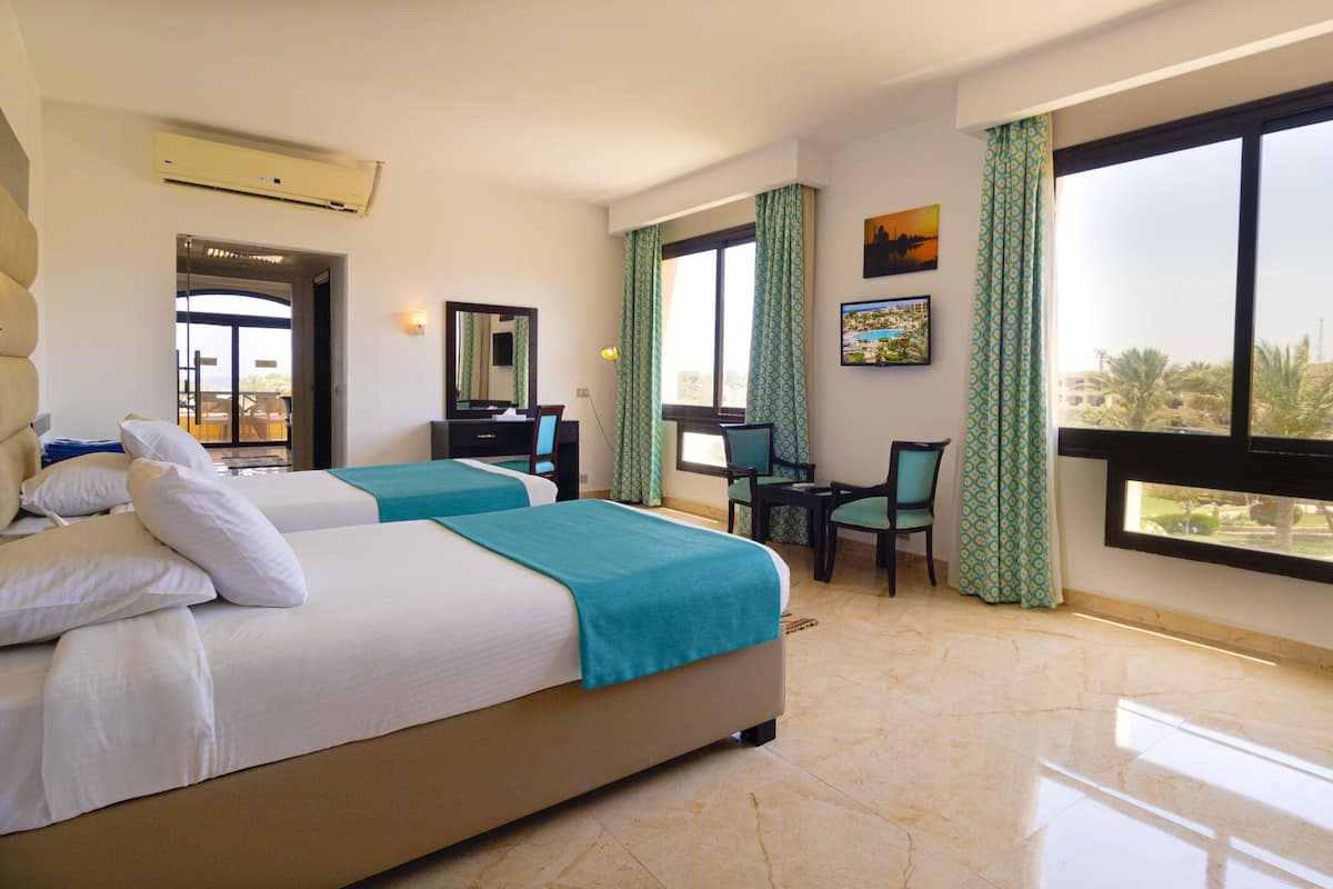 A hotel room with two beds, a desk, chairs, a large window, and a view of the city.