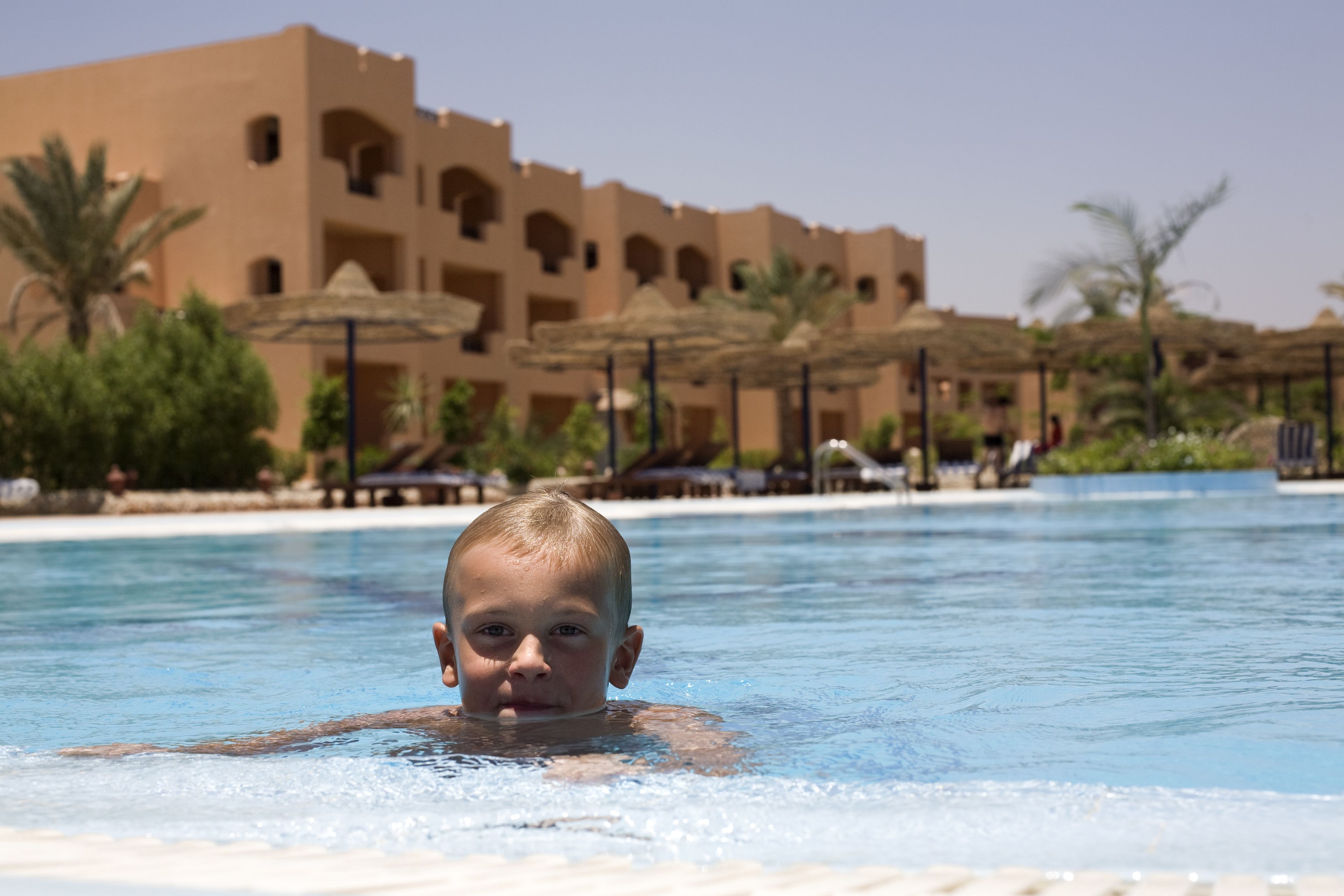 Un bambino in piscina, con un edificio di un resort sullo sfondo.