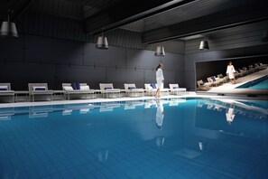 Una piscina interior con sillas de descanso y una persona caminando.