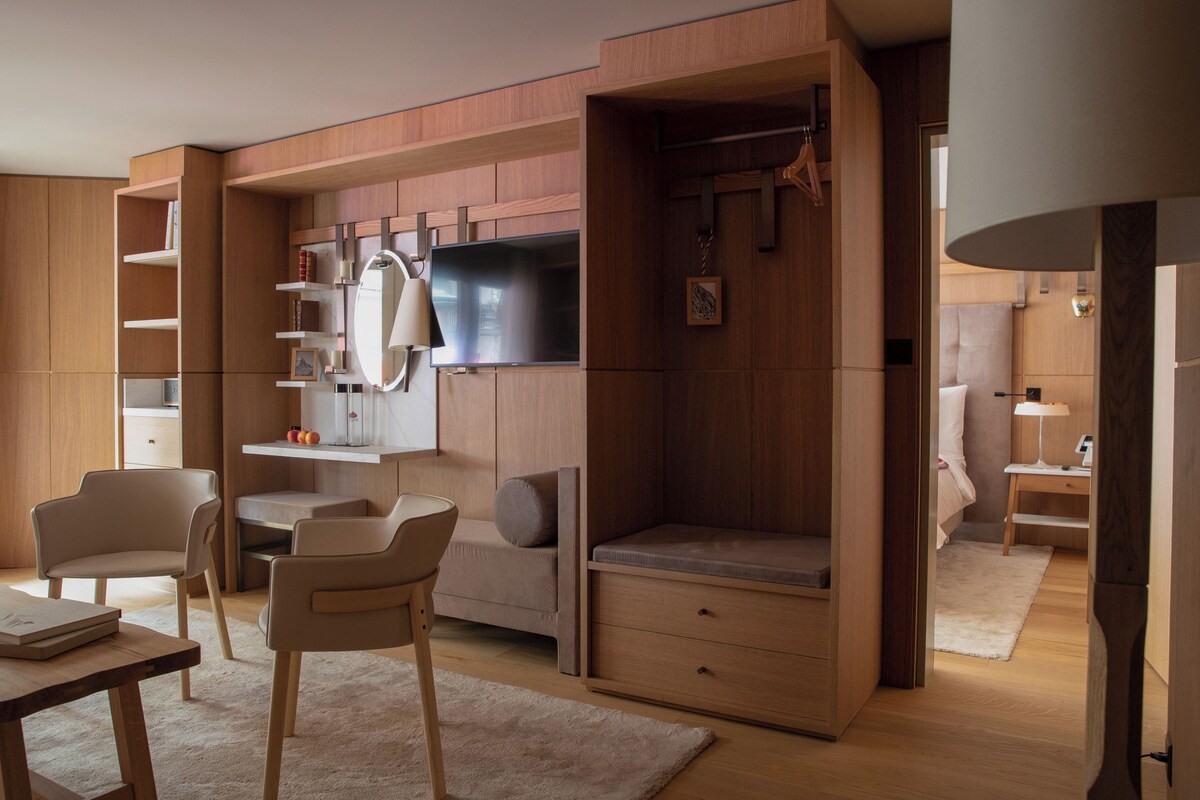 A modern bedroom with a built-in wardrobe, a flat-screen TV, and a seating area with a sofa and chairs.