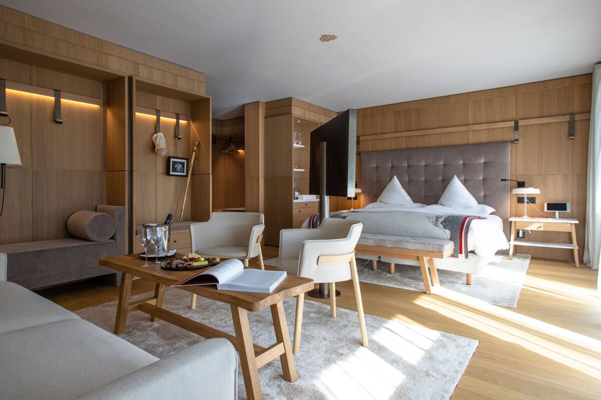 A modern hotel room with a large bed, a sofa, a dining table, and a TV.