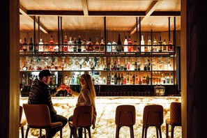 A bar area with multiple shelves of liquor bottles and glasses, wooden chairs, and a marble counter. - Schweizerhof Zermatt (Zermatt)