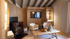 Un salón moderno con un mueble bajo para televisor de madera, dos sillas blancas, una mesa de madera con fruta y un enfriador de vino, y una estantería empotrada con cristalería.