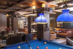 A pool table with balls, a sofa, and a bookshelf in a room with wooden ceilings and blue pendant lights. - Schweizerhof Zermatt (Zermatt)