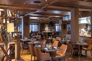 A restaurant interior with wooden beams, tables set for dining, and a bar area. - Schweizerhof Zermatt (Zermatt)